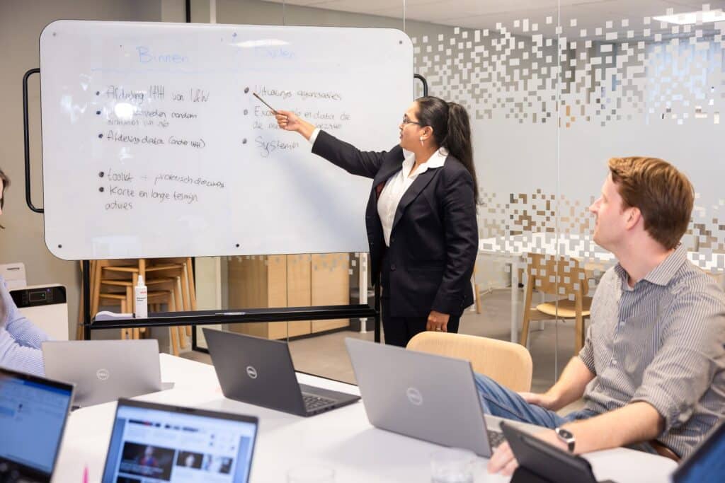 Collega geeft uitleg middels het wijzen naar een whiteboard met informatie
